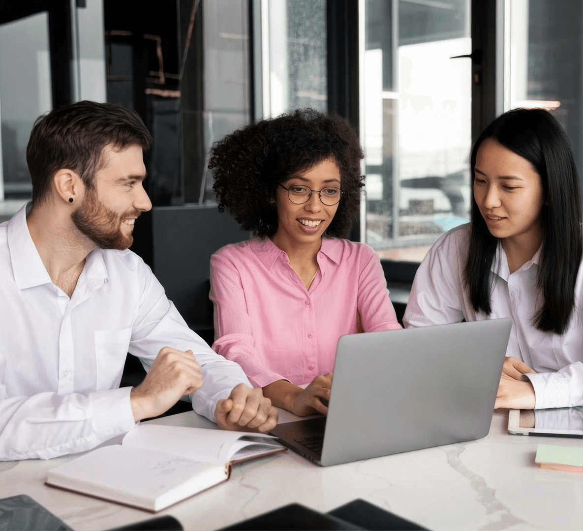 Três colegas sorrindo em volta de um notebook, numa mesa de escritório.
